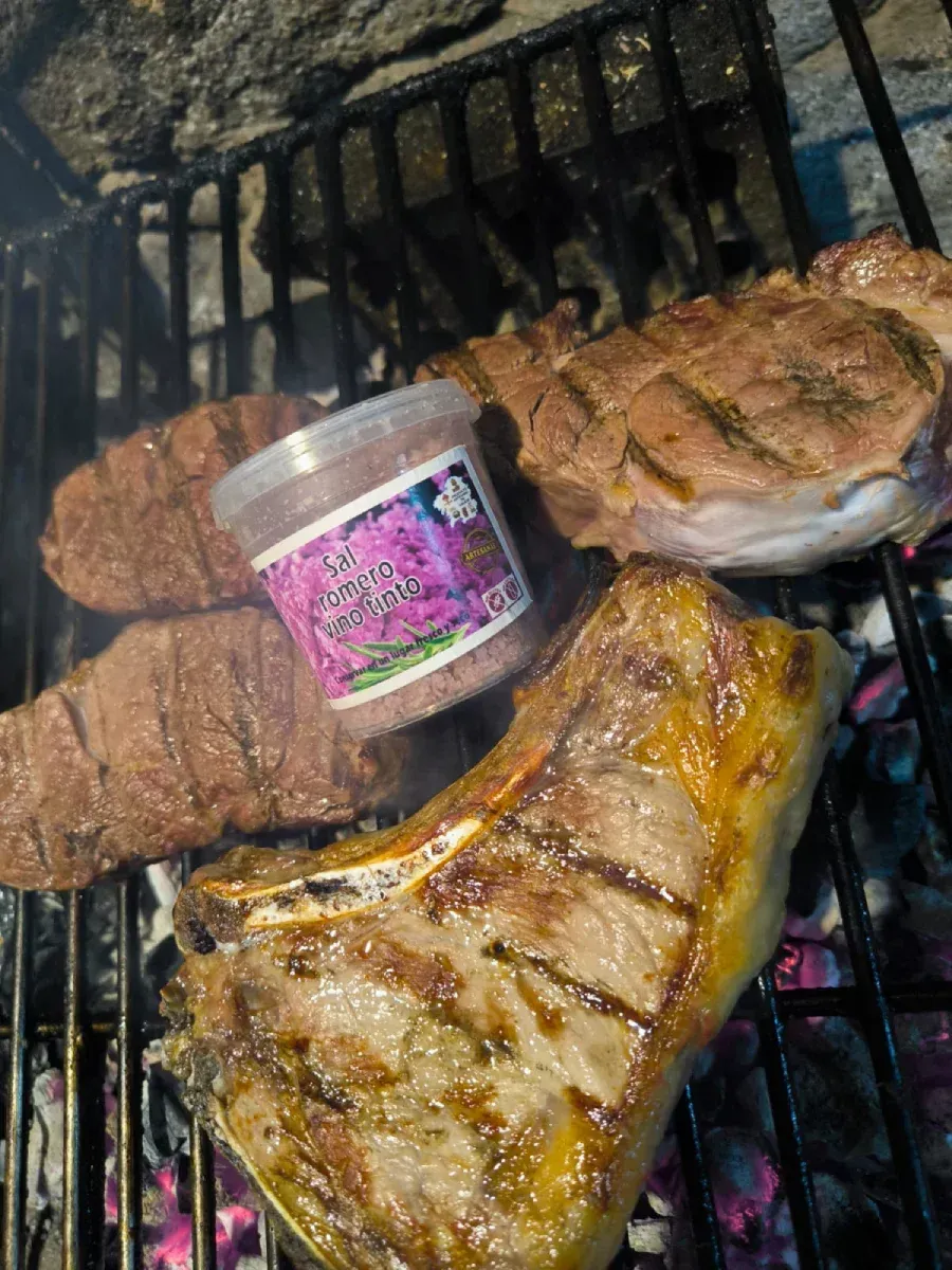 Filetes a la parrilla sobre una parrilla ahumada con un recipiente con condimento rosa.
