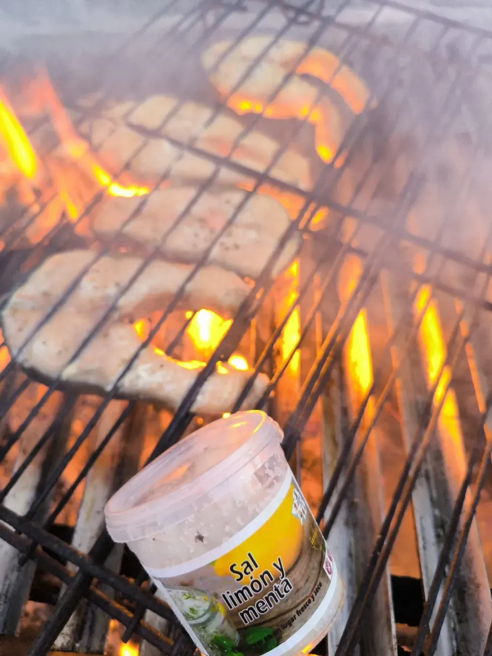 Filetes de salmón asándose sobre llamas, recipiente para condimentos 