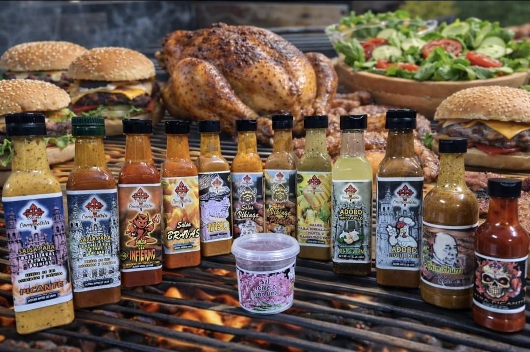 Cinco botellas de salsa picante reposan sobre una superficie de piedra con un océano y un cielo nublado de fondo.