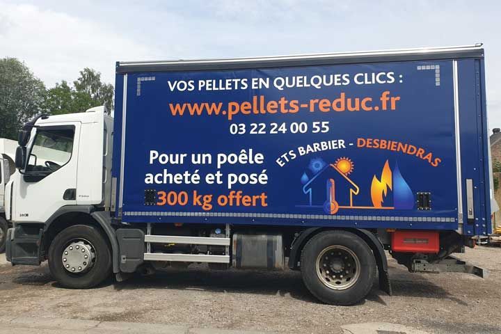 Camion de livraison blanc avec logo bleu faisant la publicité de services d'installation de poêles à bois et de granulés de bois, avec les coordonnées du prestataire.