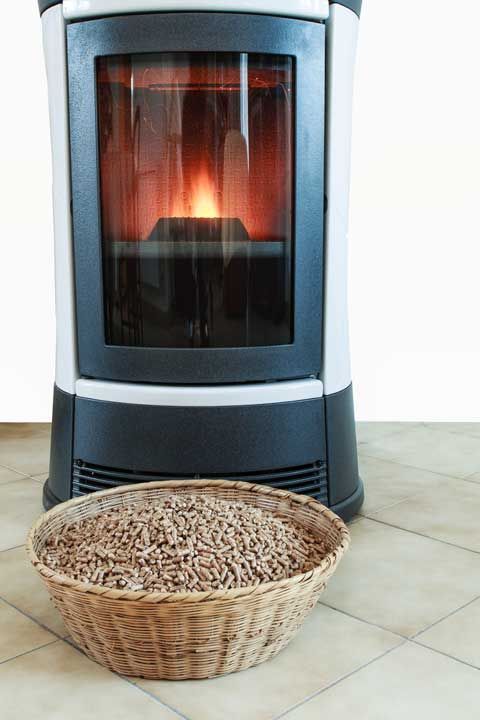 Un poêle à granulés allumé, dans un cadre blanc et noir, est posé sur un sol carrelé, avec un panier en osier rempli de granulés de bois au premier plan.