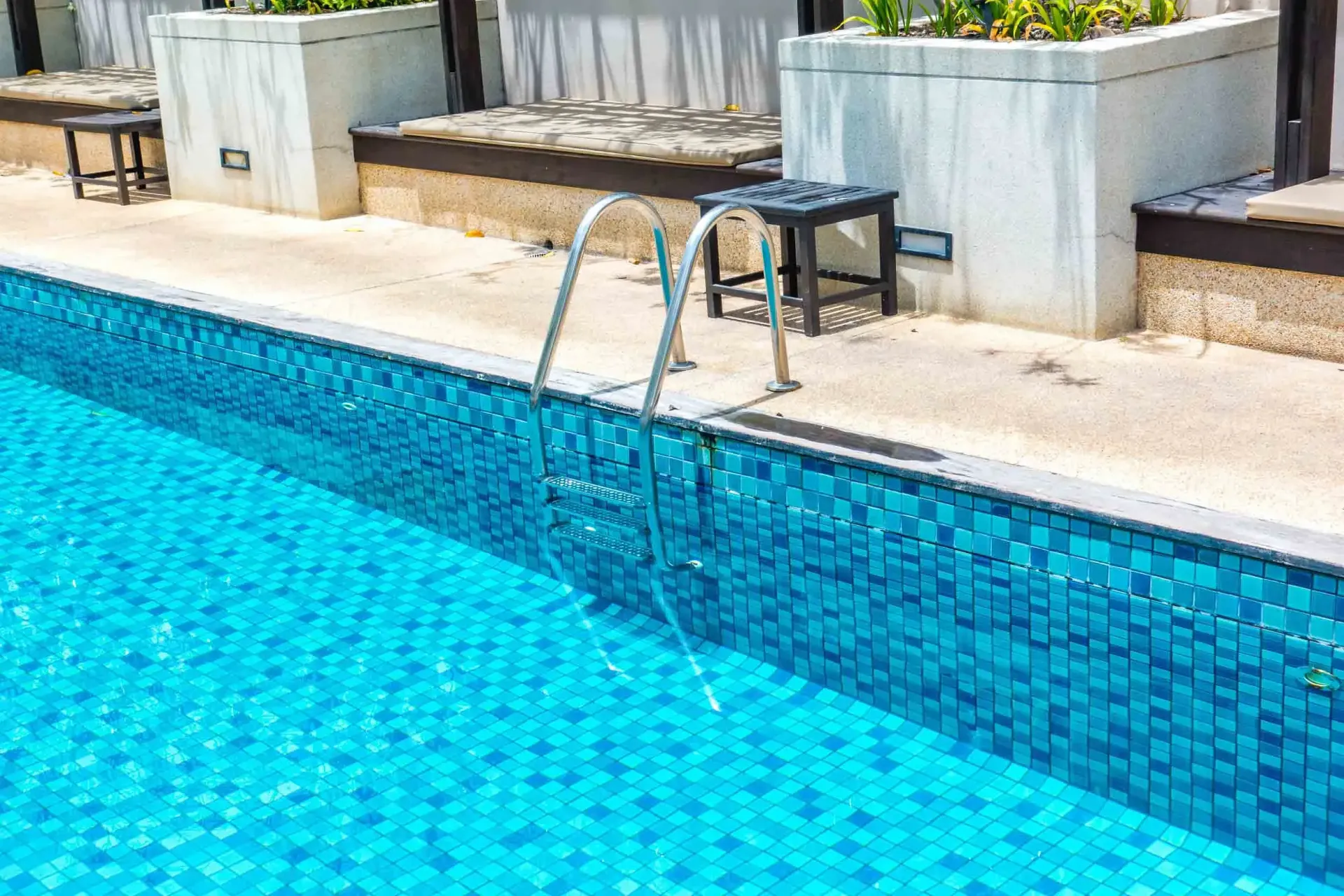 Piscina con azulejos azules y escalera. Junto a un patio y un edificio.