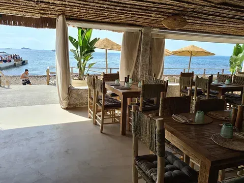 Mesas de restaurante con vista al mar y techo de paja. Sillas y mesas de madera. Día soleado.