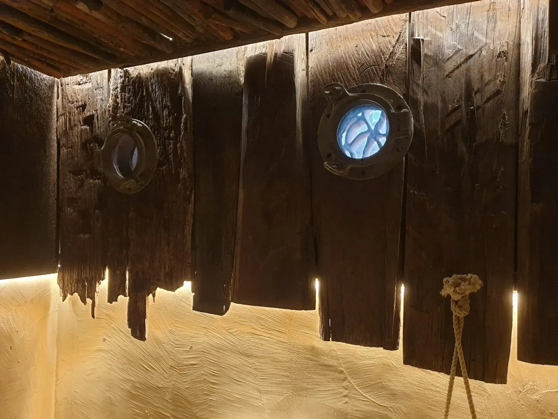 Pared de madera desgastada con dos ventanas de ojo de buey, iluminadas desde atrás, y una cuerda.