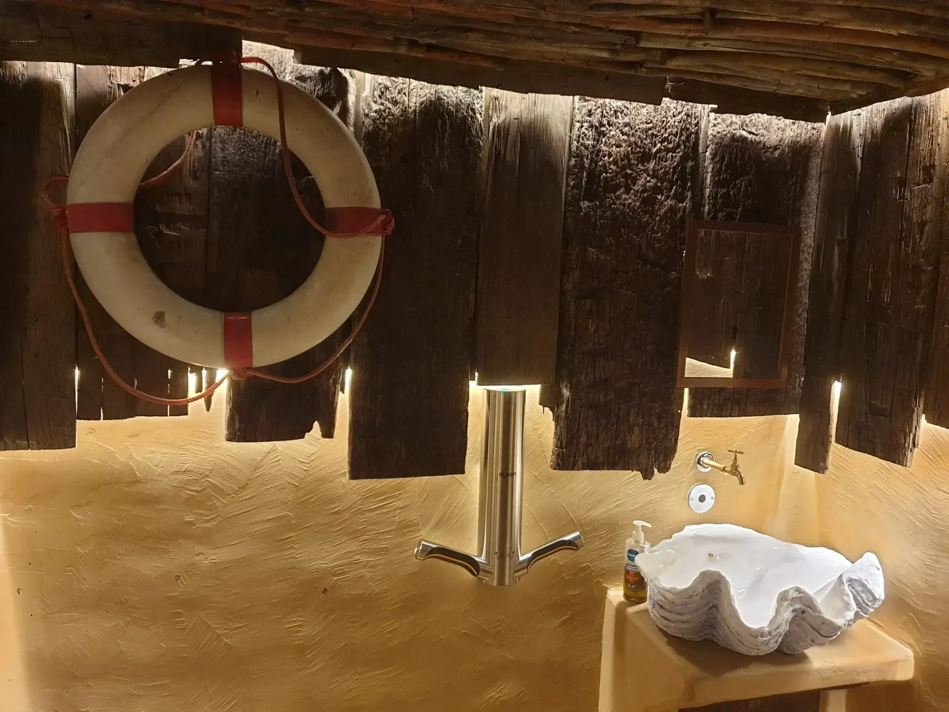 Baño con paredes de madera, salvavidas, lavabo de concha y grifo cromado.