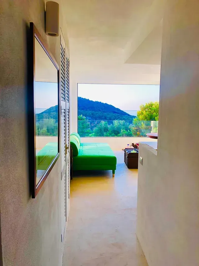 Un sofá verde en una habitación moderna ofrece vistas a la montaña. Un espejo cuelga de la pared.