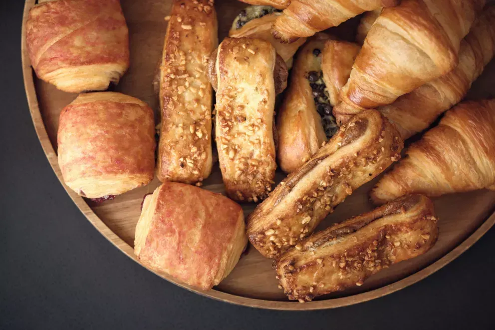 A wooden tray filled with a variety of pastries and croissants.