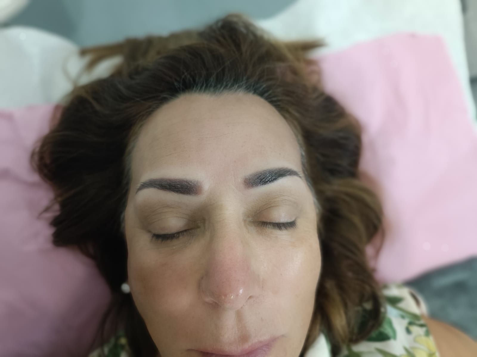Mujer con ojos cerrados, cejas recién tatuadas, cabello castaño, tumbada sobre una almohada rosa.