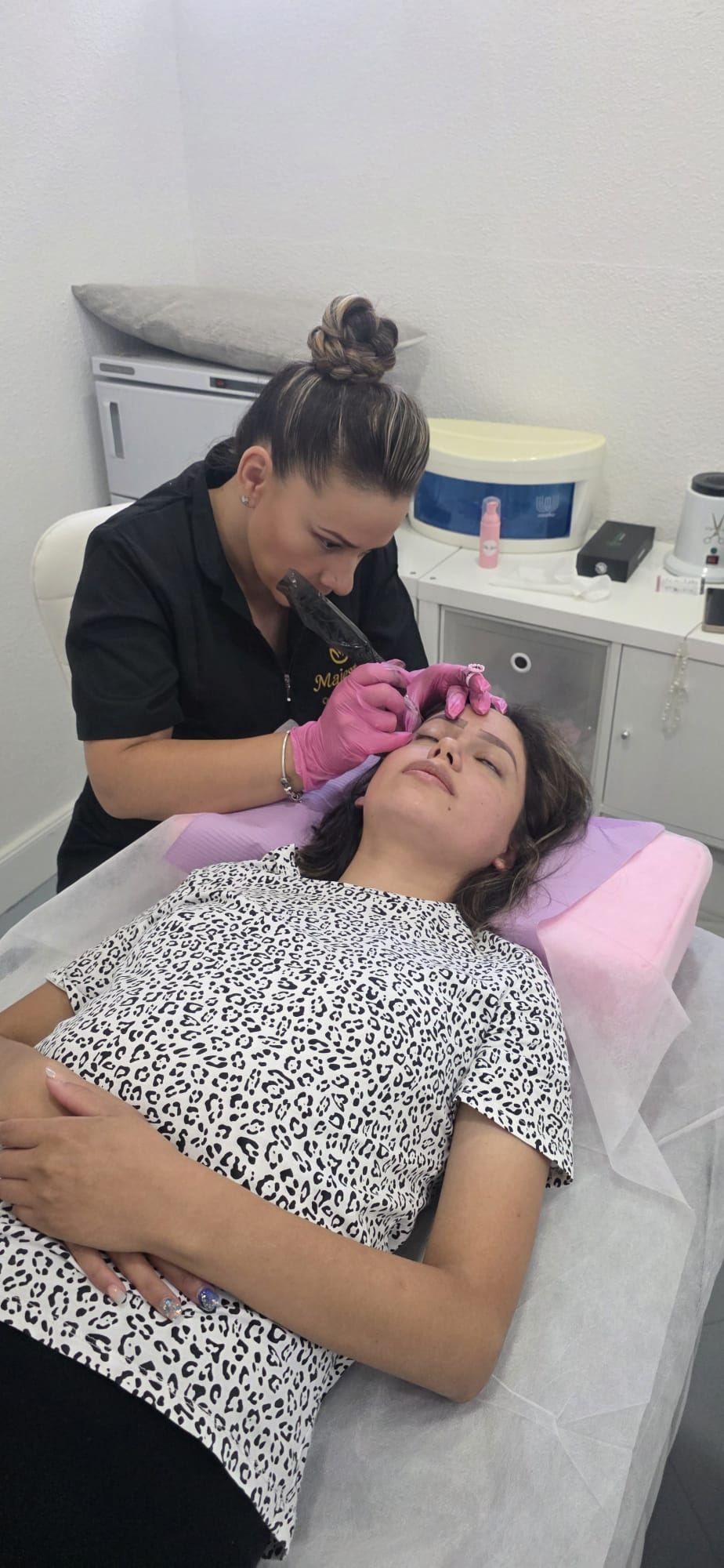 Mujer recibiendo un procedimiento de cejas por parte de un profesional en un salón.