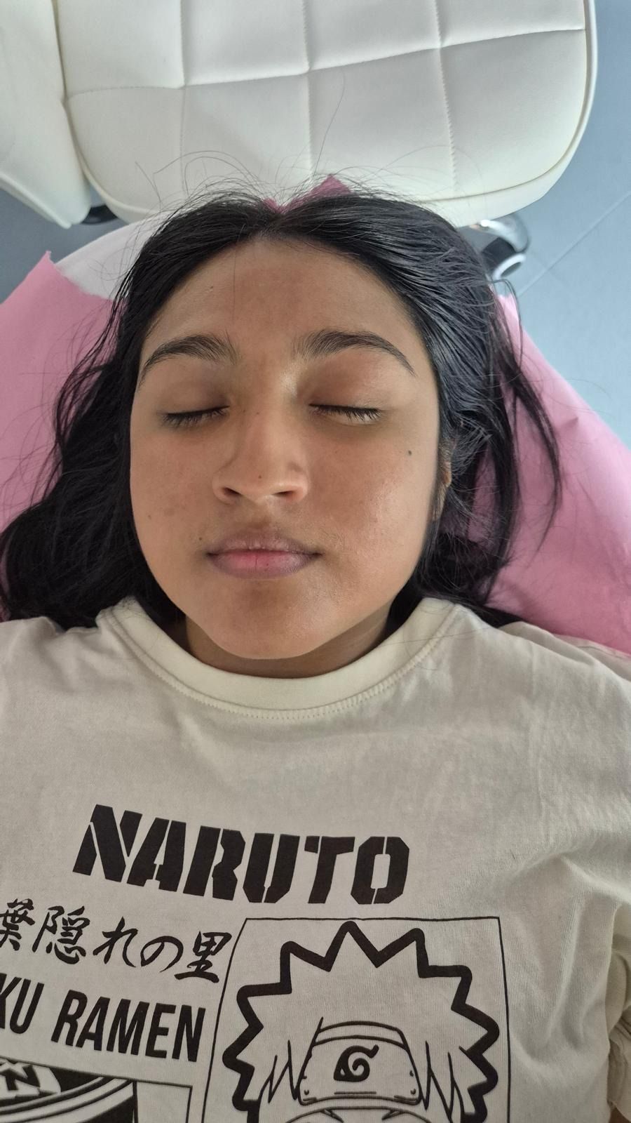 Mujer con los ojos cerrados, vistiendo una camiseta de Naruto, tumbada sobre una almohada rosa.