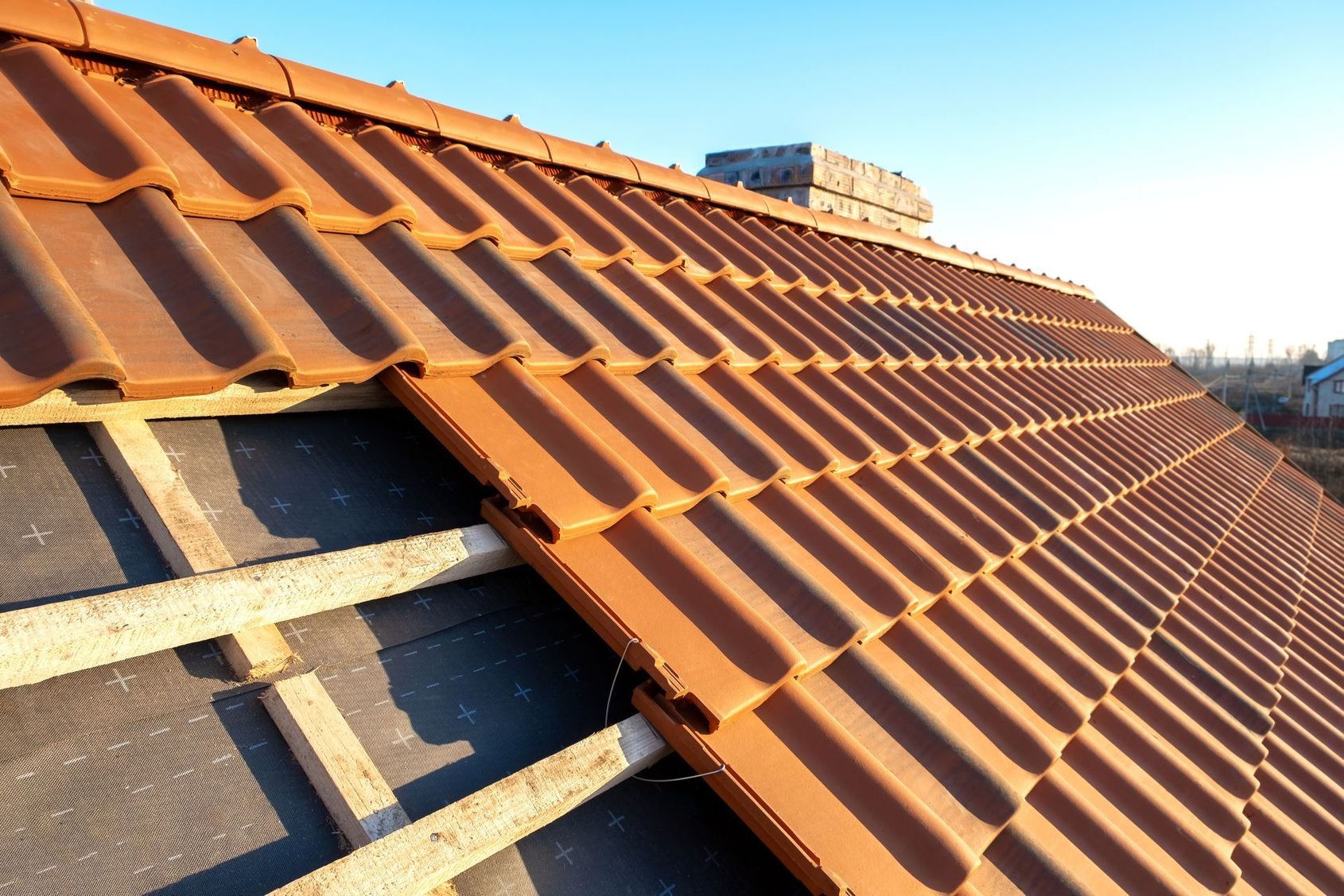 Gros plan sur une toiture en tuiles de terre cuite en construction, avec sous-couche apparente et linteaux en bois.