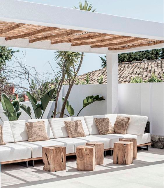 Un patio con un sofá y taburetes de madera bajo una pérgola.