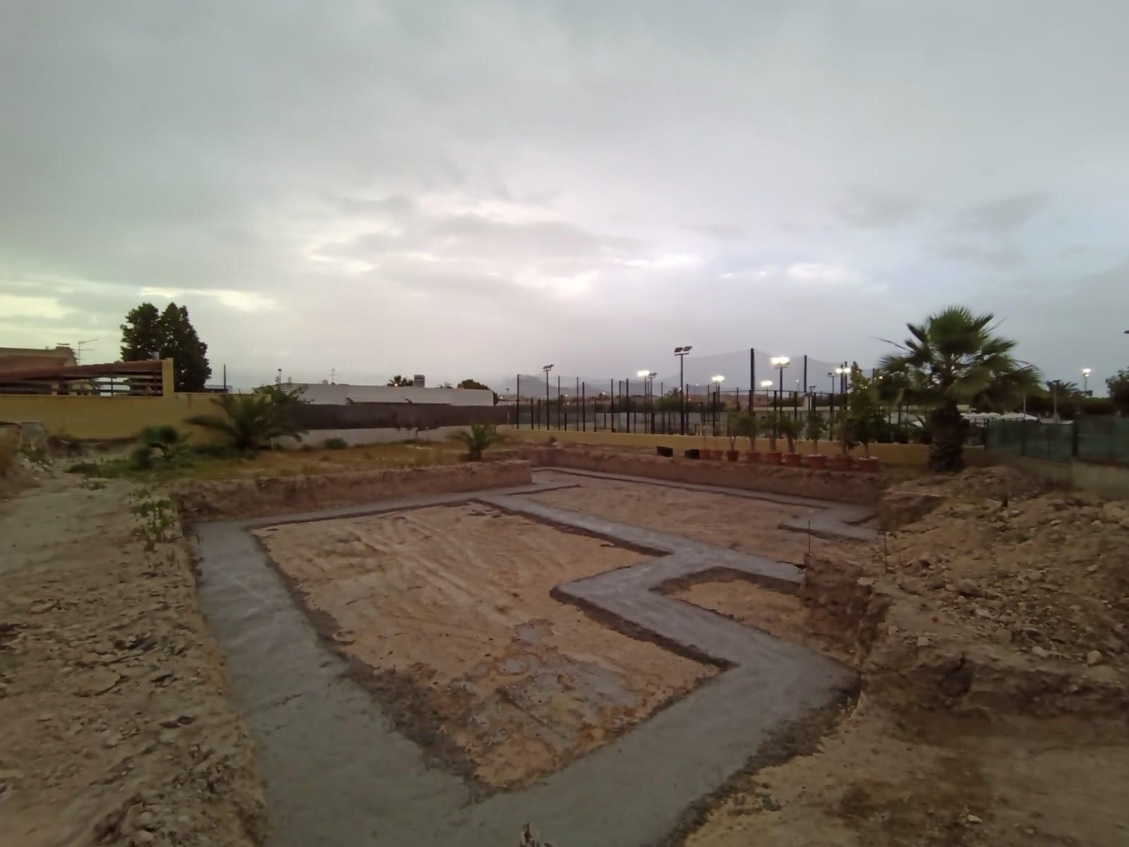 Terreno en construcción vacío con una gran base de hormigón y suelo fangoso bajo cielos nublados.
