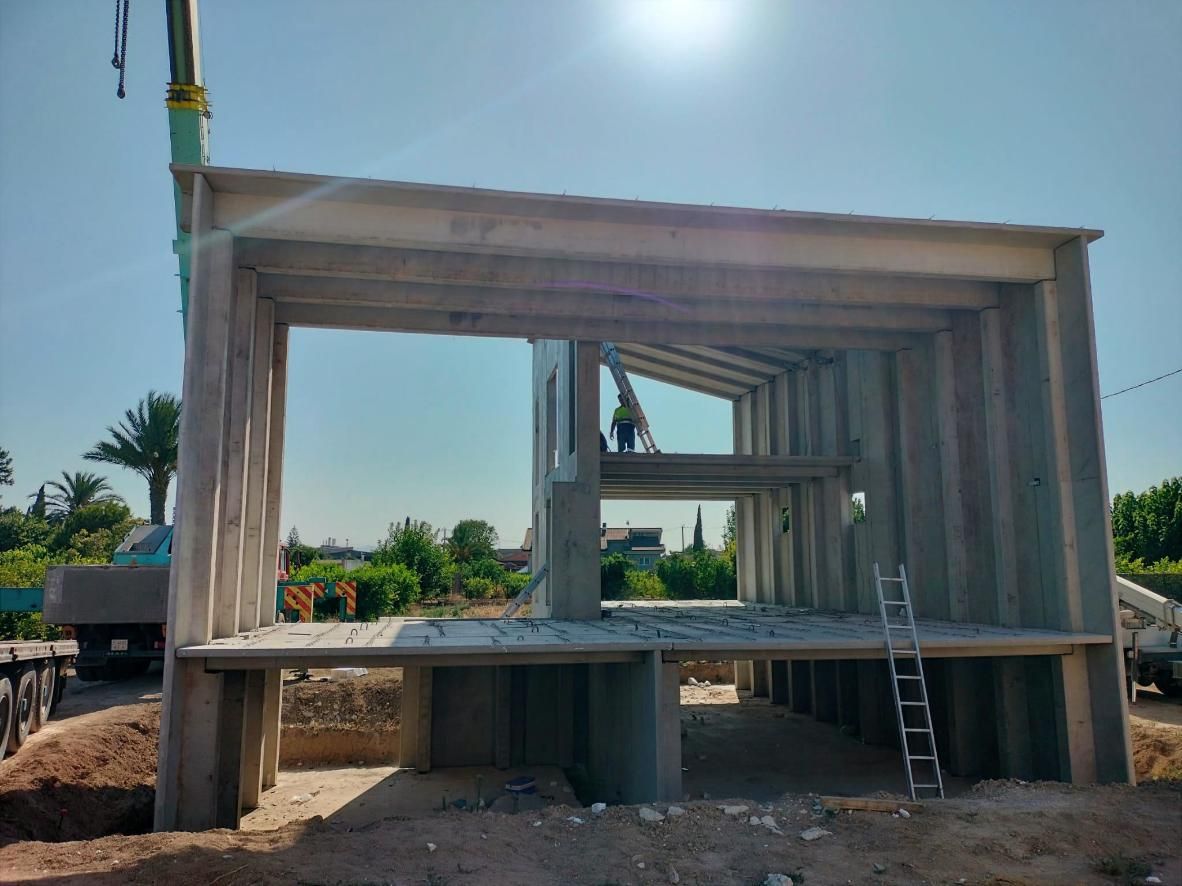 Estructura de hormigón parcialmente construida con trabajadores, escalera y cielo azul brillante.