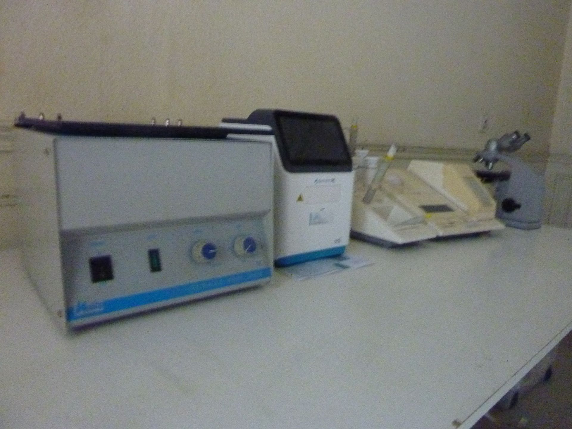 Équipement de laboratoire : centrifugeuse, analyseur, microscope sont posés sur une paillasse blanche dans un laboratoire.