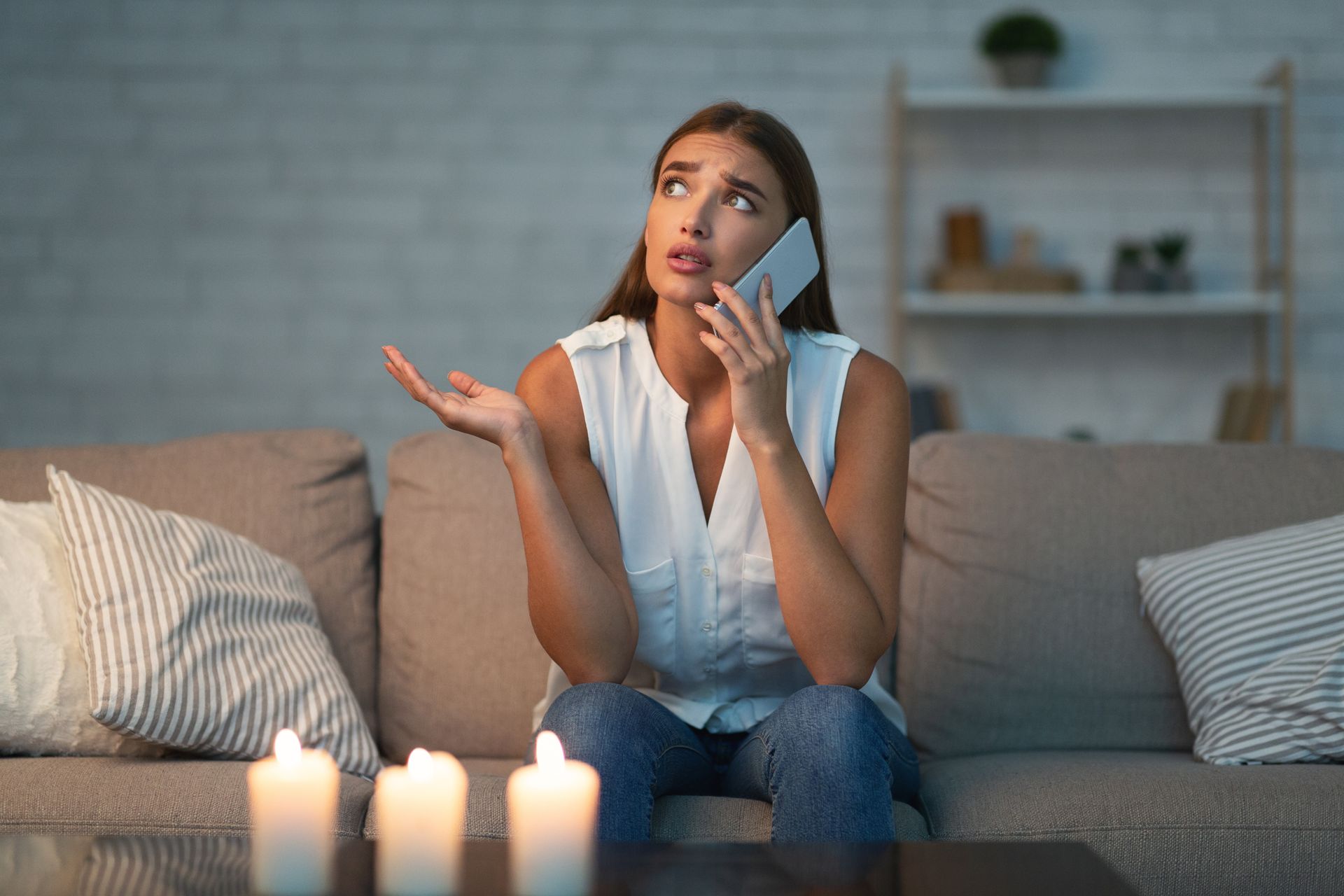 Une femme assise sur un canapé, tenant un téléphone avec des bougies allumées devant elle.