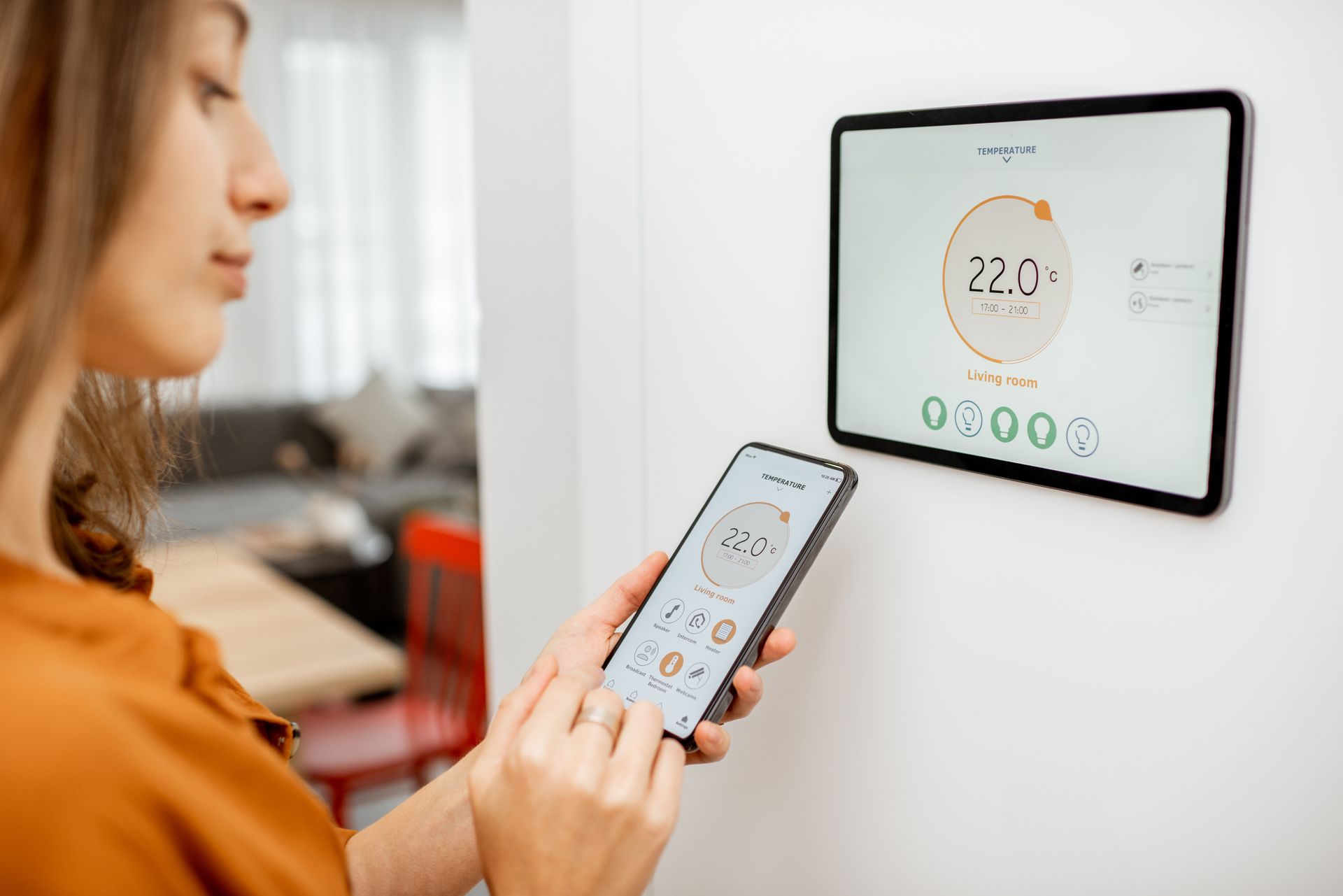 Une femme consultant une application de domotique sur son téléphone et une tablette murale