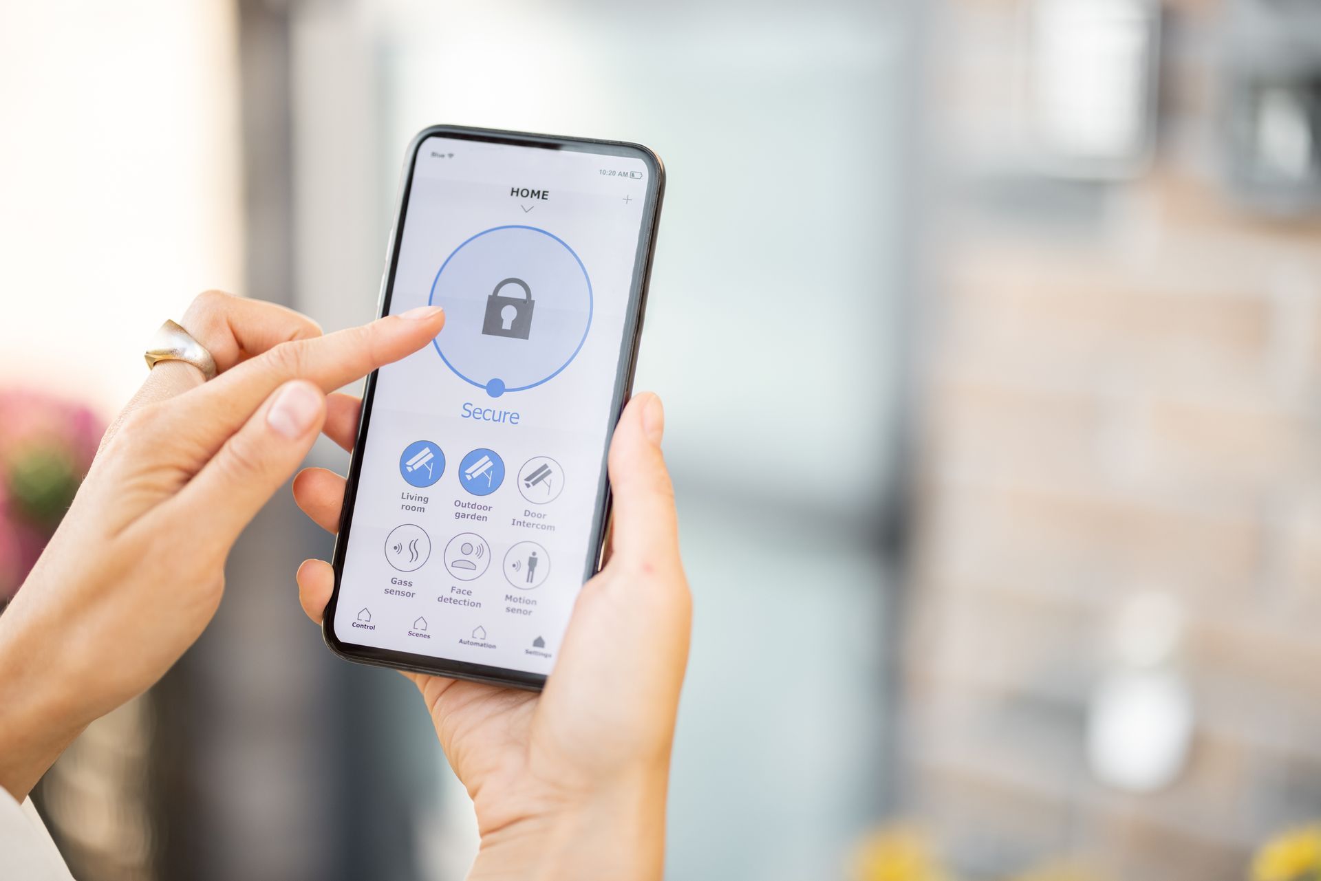 Des mains tenant un smartphone avec une application de sécurité ouverte, affichant une icône de verrouillage et des icônes de paramètres.