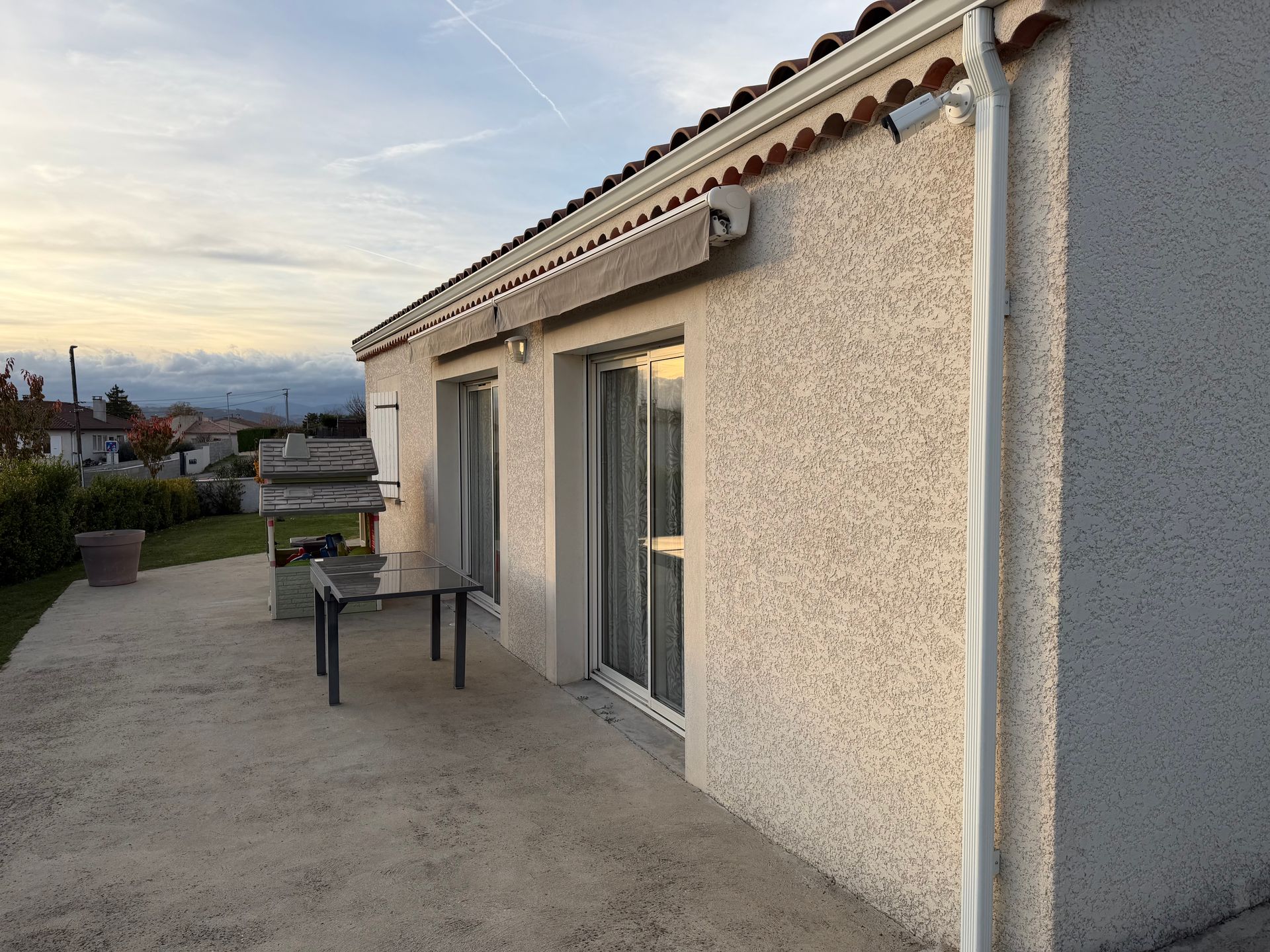 Patio d'une maison en stuc au coucher du soleil, avce une caméra de surveillance sur la façade.