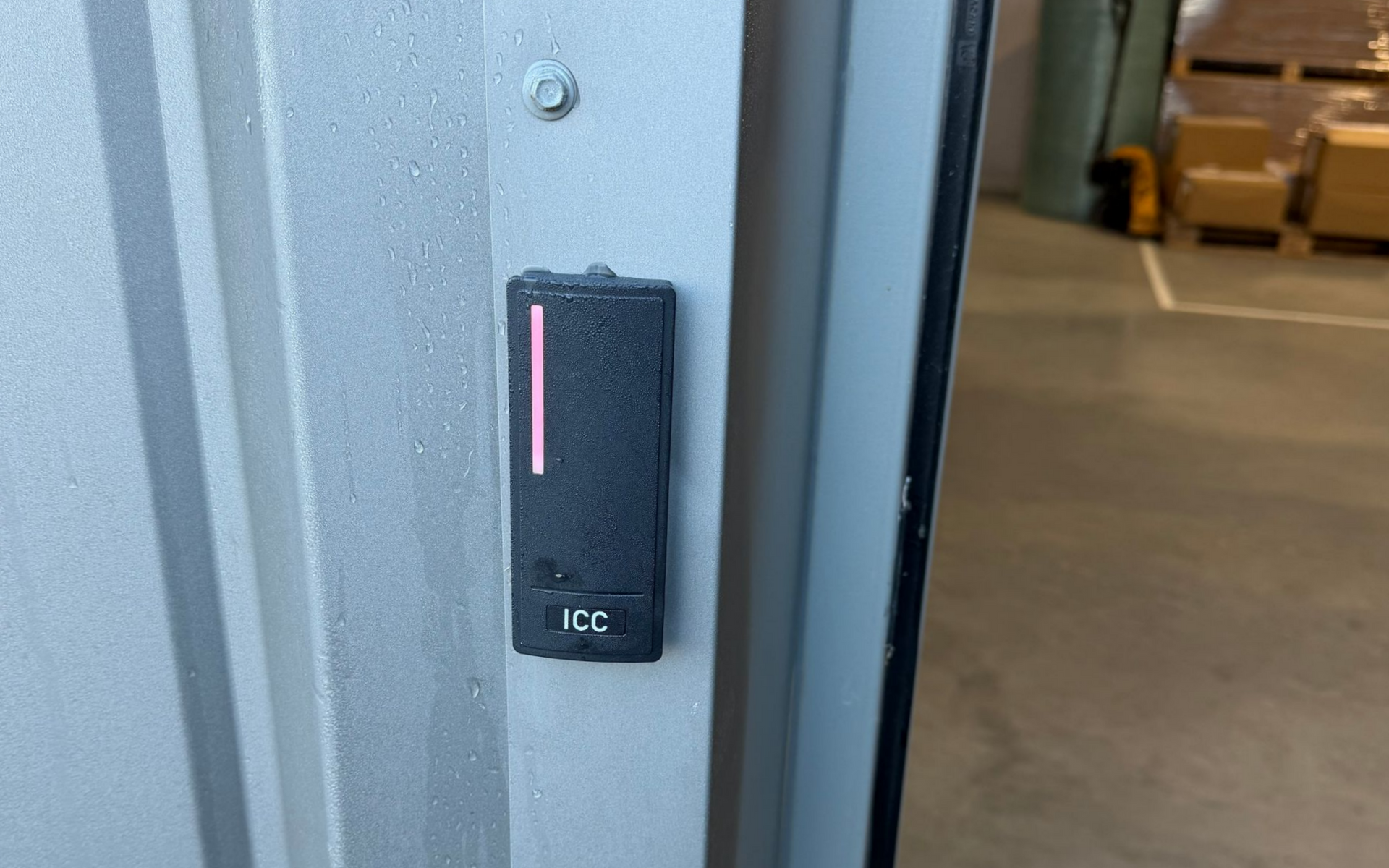 Bouton d'accès mural noir avec voyant lumineux rose, situé à côté d'une porte.