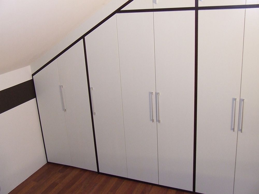 Ein Raum mit Dachschräge und weißen Schränken