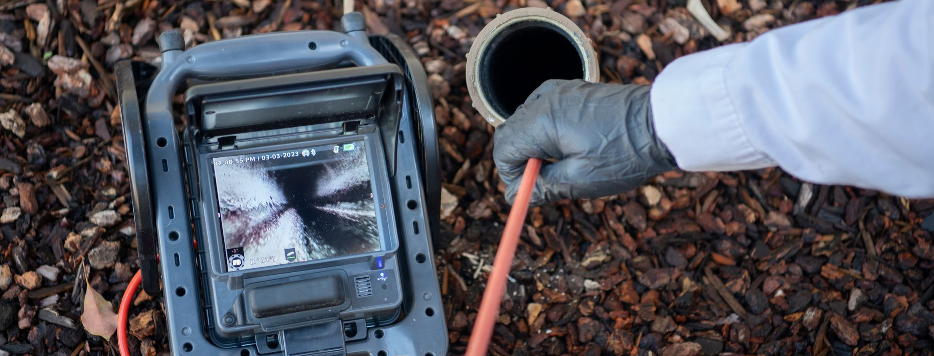 Une personne portant des gants et un uniforme blanc inspecte un tuyau avec une caméra.