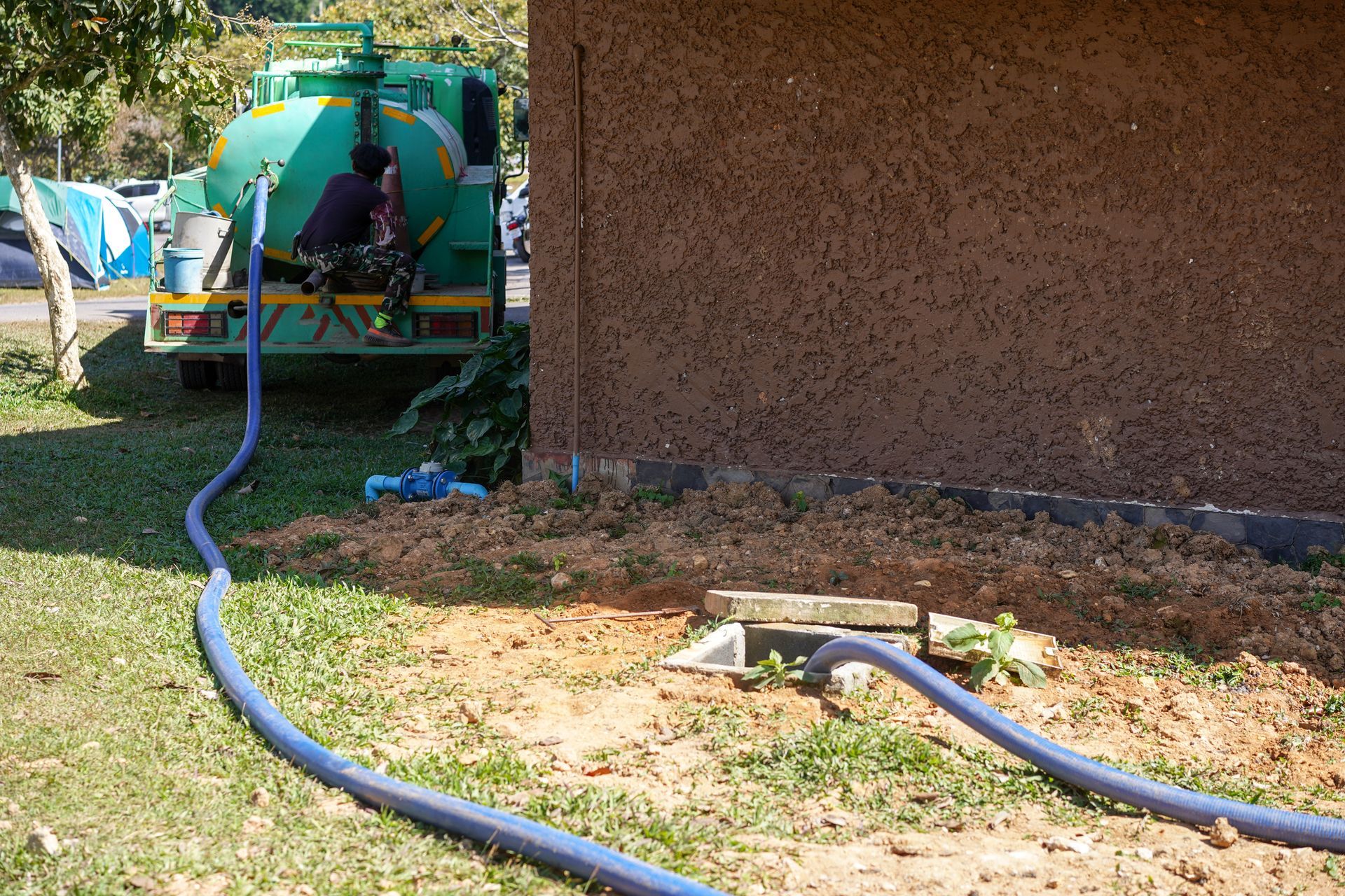 Camion de vidange de fosse septique en train de vider une fosse à côté d'un bâtiment.