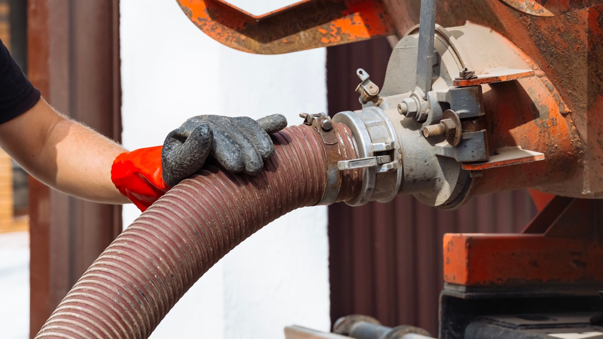 Une personne, portant des gants, raccorde un gros tuyau marron à un camion de vidange.