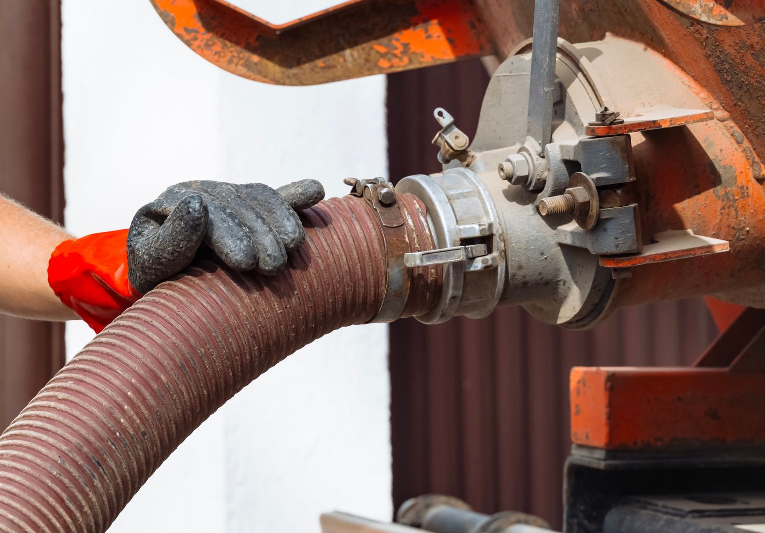 Une personne portant des gants de travail raccorde un gros tuyau à un camion de vidange.