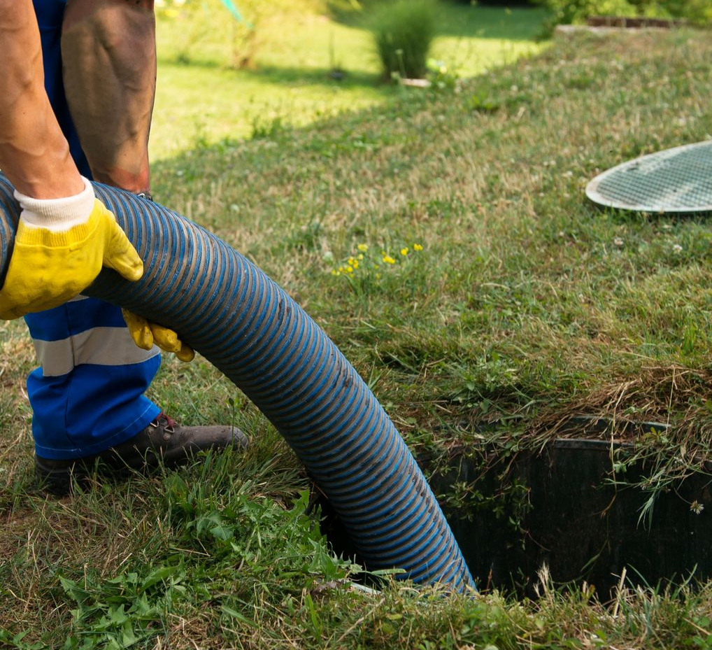 Une personne en tenue de travail et gants vide une fosse septique à l'aide d'un gros tuyau.