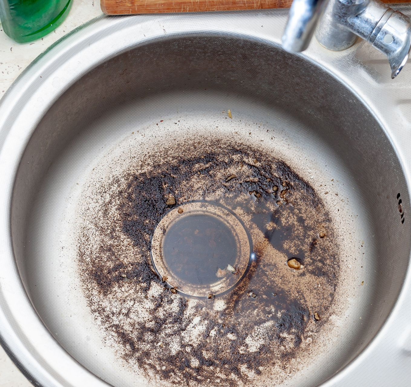 Évier de cuisine en acier inoxydable sale, avec des dépôts de crasse autour de la bonde.