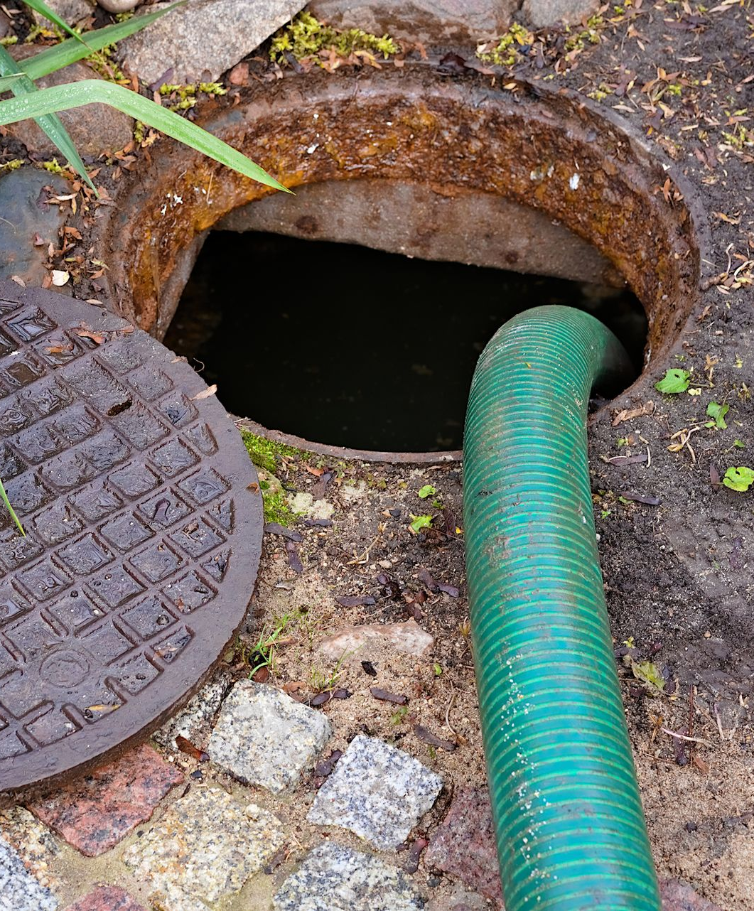 Accès aux égouts à ciel ouvert avec un tuyau vert à l'intérieur.