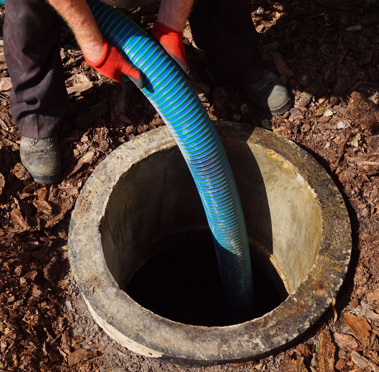 Un homme utilise un tuyau bleu pour vider une fosse septique.