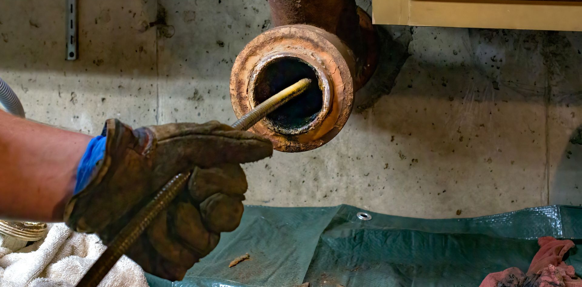 Une personne portant des gants utilise un outil pour nettoyer un tuyau rouillé.