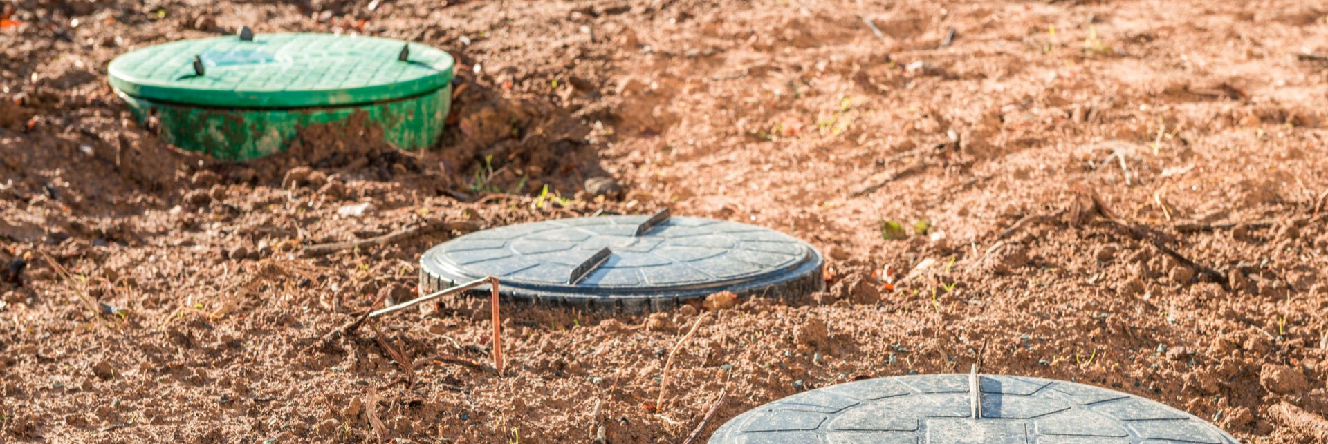 Trois fosses septiques couvertes dans un terrain vague en terre.