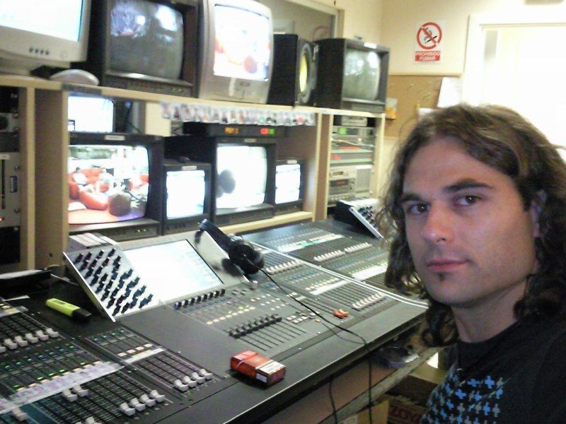 Hombre en una consola de transmisión con varios monitores en un estudio poco iluminado.