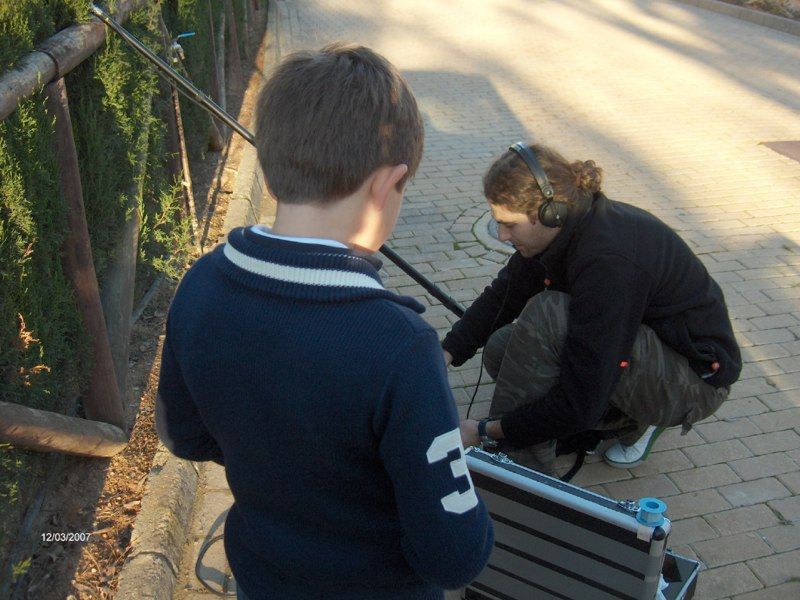 Niño con suéter azul marino; persona ajustando equipo de sonido, ambientación de acera.