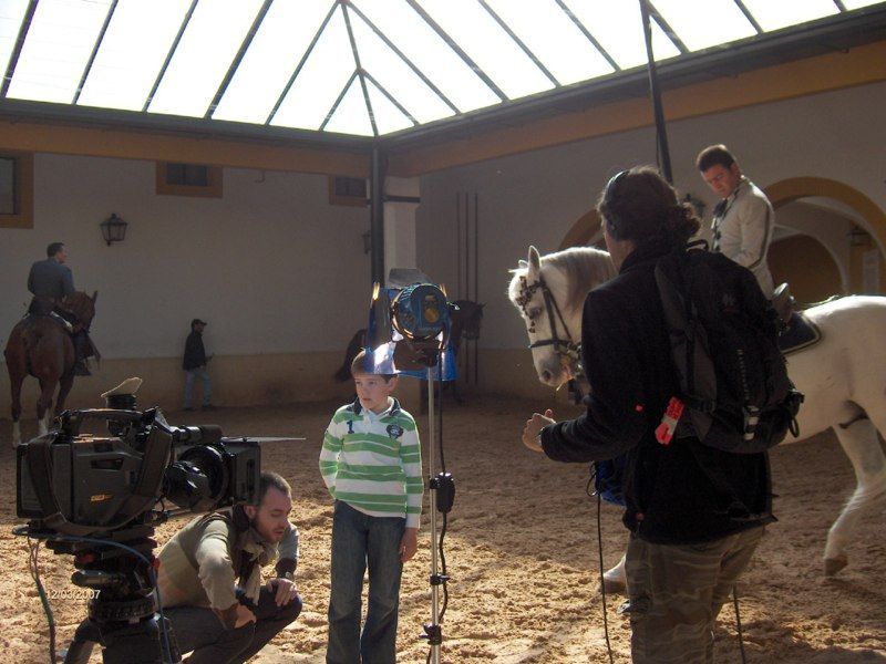 Equipo de filmación filmando a un niño con un caballo en el interior; luz solar, suelo de arena.