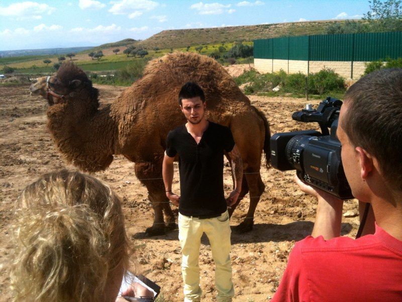 Un hombre posa con un camello para el equipo de cámara al aire libre.