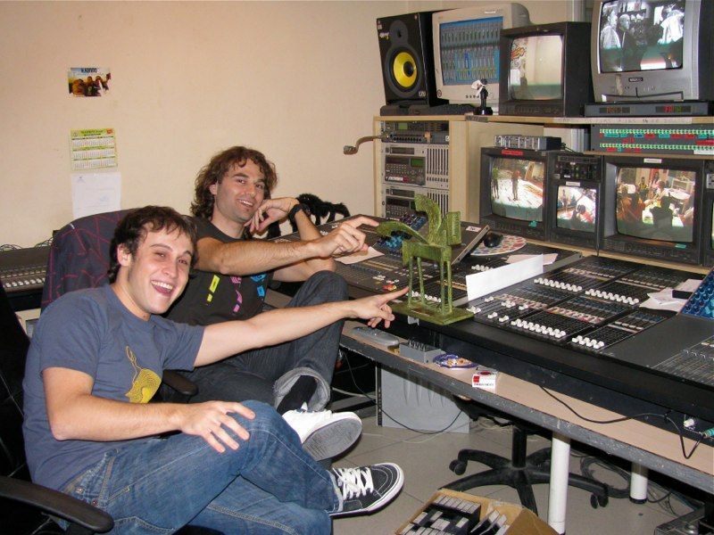 Dos hombres sentados en una sala de edición de vídeo, apuntando a un equipo con monitores que muestran vídeo.