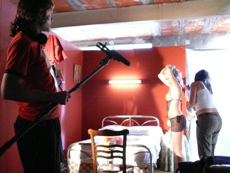 Una persona sostiene un micrófono de brazo hacia dos personas en un set de filmación en una habitación roja.