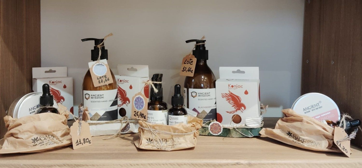 Un estante de madera exhibe una variedad de productos para el cuidado de la piel en frascos de color ámbar, cajas blancas con gráficos rojos y empaques de papel.