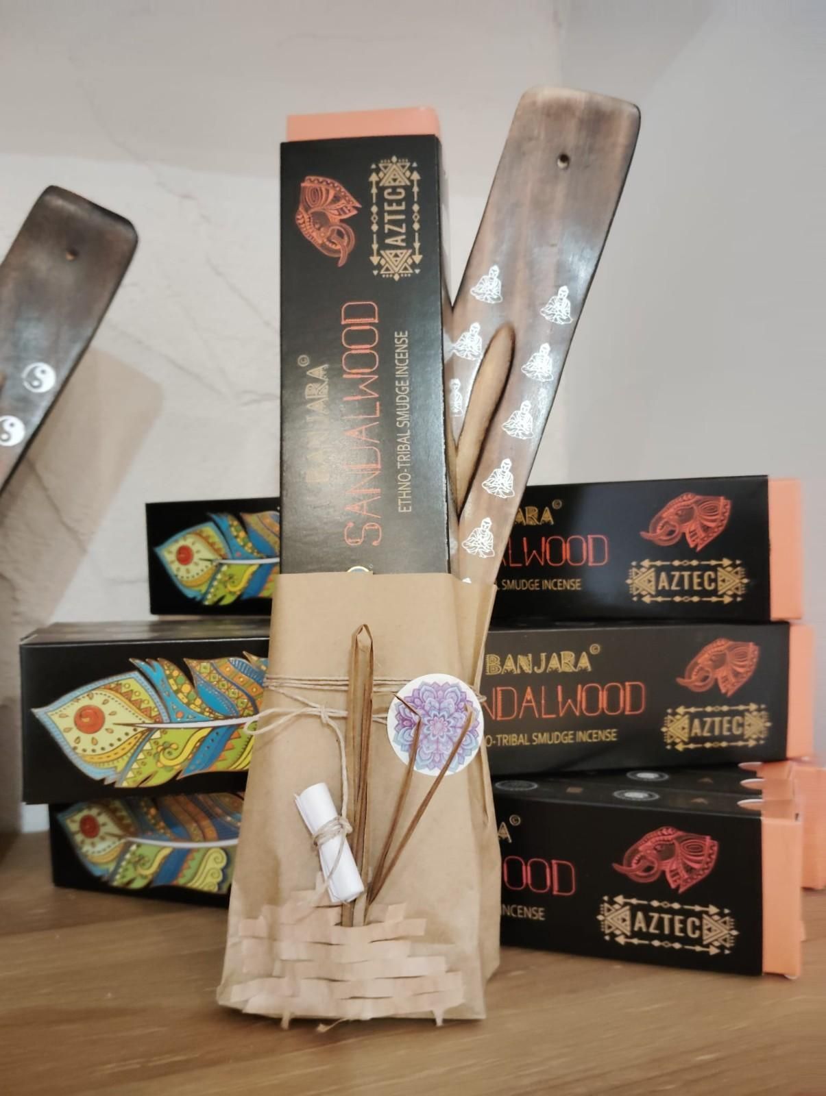 Un porta incienso de madera y varias cajas de incienso de la marca Sandalwood apiladas detrás de un set de regalo envuelto sobre una mesa de madera.