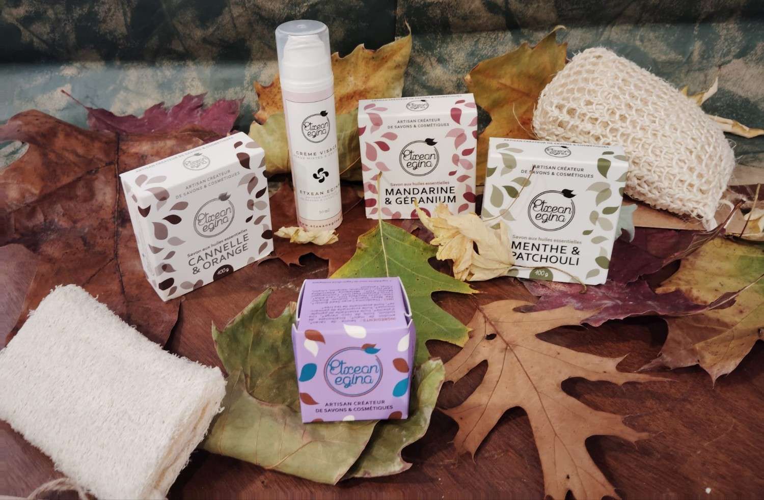 Una colección de productos de belleza y cuidado de la piel dispuestos sobre hojas otoñales, que incluye varias cajas, un frasco con dosificador y esponjas.