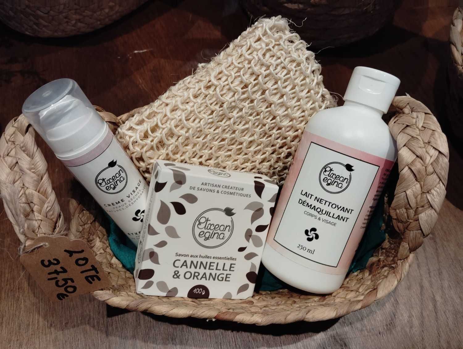 Una cesta tejida que contiene un frasco con dosificador, una pastilla de jabón de canela y naranja, un frasco de loción y una esponja de baño natural.