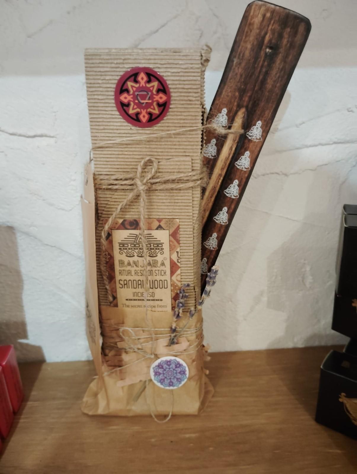 Un paquete de regalo de cartón con cordel, etiquetas y un abanico de madera con dibujos blancos colocado junto a él sobre una mesa de madera.