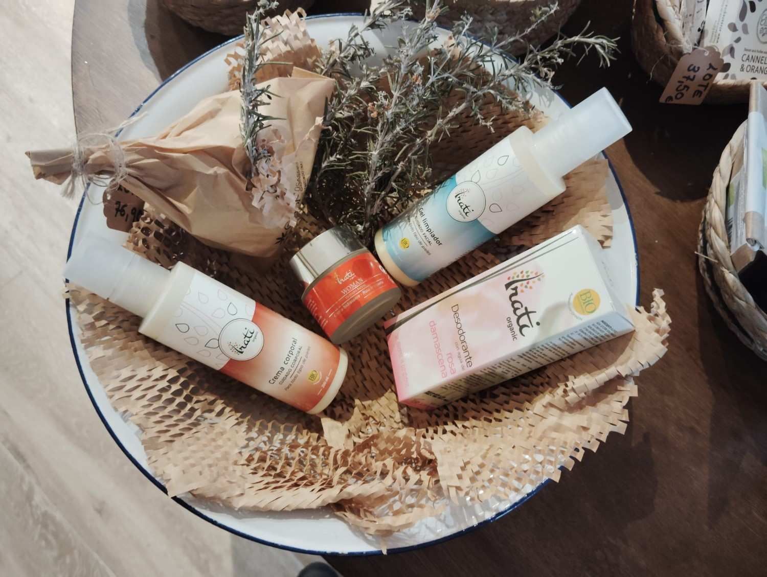 Una cesta repleta de productos para el cuidado de la piel de la marca Pruti, que incluye frascos, un tarro de crema y un artículo envuelto para regalo con hierbas secas.