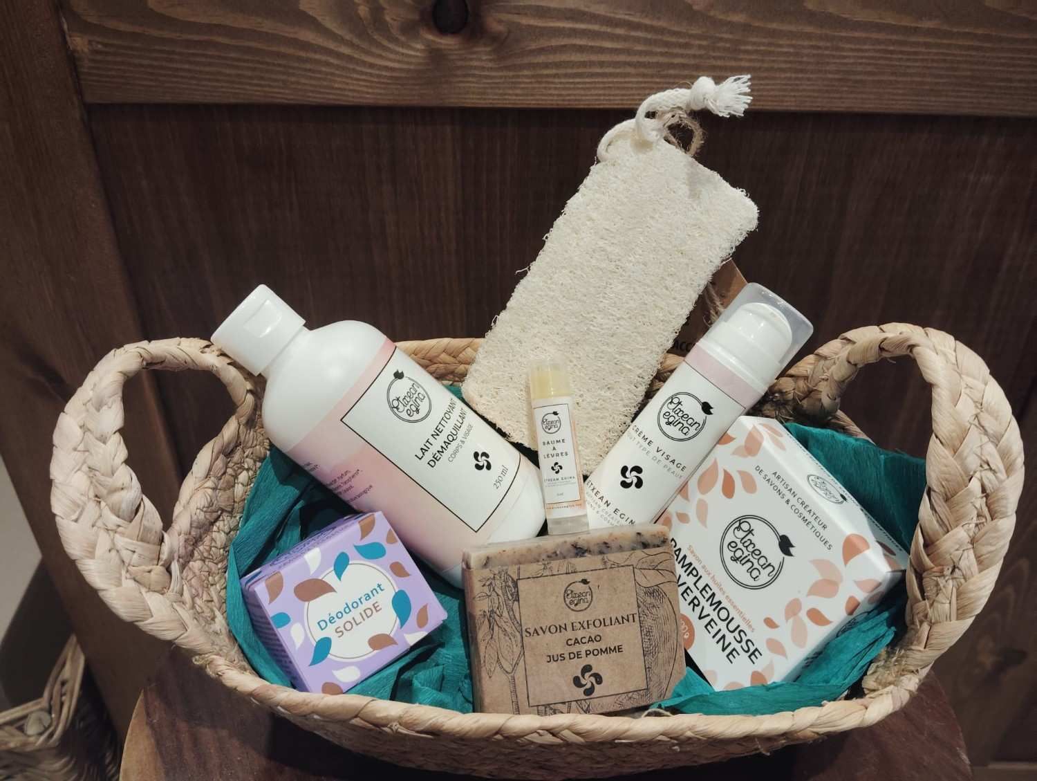 Una cesta tejida que contiene varios productos para el cuidado de la piel, una pequeña pastilla de jabón y una almohadilla exfoliante.