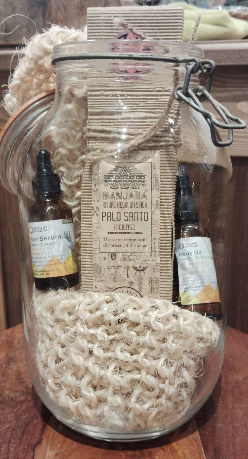 Un frasco de vidrio lleno con dos frascos cuentagotas marrones, un manojo de palo santo envuelto y un paño de tela tejida de color canela.