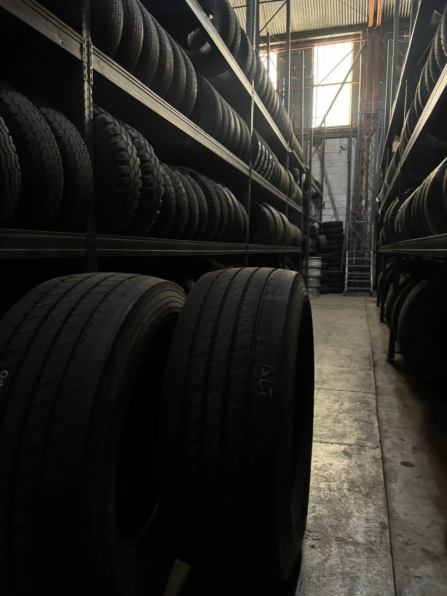 Filas de neumáticos almacenados en estantes de metal en un almacén poco iluminado.